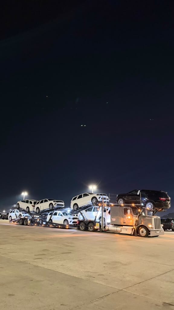 Car carrier loaded with white SUVs at night