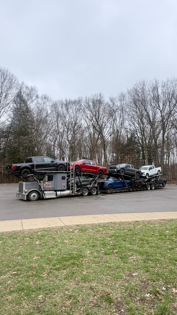 Car carrier loaded with pickups by a tree line